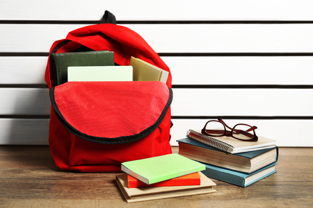 Red backpack with books and glasses on wooden background