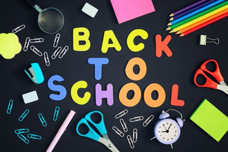 On a black background there are paperclips a notebook an alarm clock and school supplies in the center the inscription in colored letters back to school Stock Photo