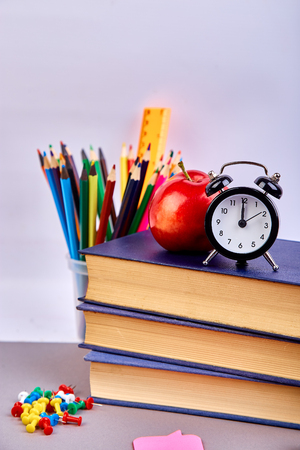 Back to school supplies books and red apple on green background still life with alarm clock copy space