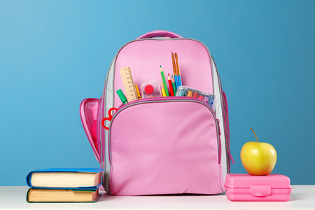 Student set pink backpack with stationery a stack of books a lunchbox an apple on the table on a blue background back to school Stock Photo