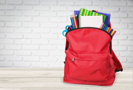 Backpack with school stationery on table against brick wall