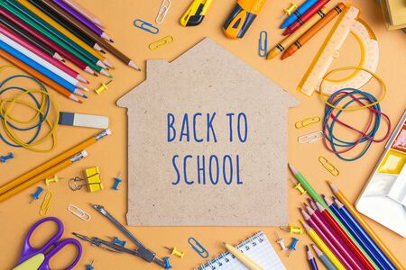 Back to school concept with house symbol and school supplies on yellow background top view