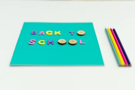 Turquoise notepad with text back to school laid on it colored pencils by the side isolated