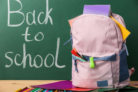 Backpack and stationery against blackboard with text back to school Stock Photo