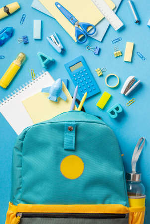 Back to school concept top view vertical photo of school supplies flying out of blue schoolbag on isolated blue background Stock Photo