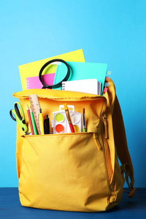 Yellow backpack and different school stationery on blue wooden table