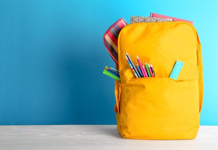 Backpack with different colorful stationery on table back to school