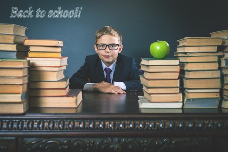 Back to school smart school boy sitting at the table with many books child dressed in school uniform and glasses Stock Photo