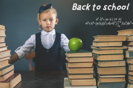 Back to school smart school girl reading a book at library mathematical formula at blackboard table with many books and one green apple student concept of education Stock Photo