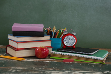 Stack of books with alarm clock apple and pen holder on wooden table