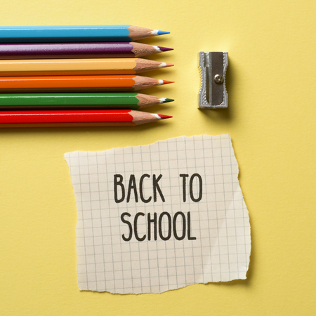 High angle shot of some pencil crayon of different colors a metallic sharpener and a note with the text back to school on a yellow background Stock Photo