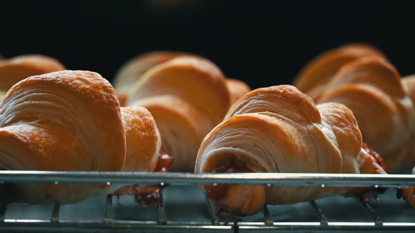 Fluffy stuffed croissants sprinkled with powdered sugar in slow mo. Close-up pastries are decorated with powdered sugar. Homemade delicious pastries. Puff pastry and buns with sweet filling.